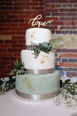Üzerinde aşk harfleri olan beyaz ve yeşil renkli canlı bitkilerle süslenmiş üç katlı güzel bir düğün pastası. Kutlama pastası..
