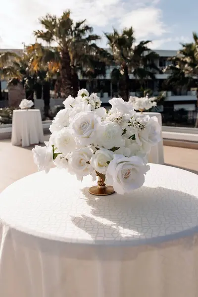An elegant dining table decorated with a bouquet of white roses, a beautiful festive setting outside. Beautiful outdoor table setting with white flowers for a dinner, wedding or other festive event.