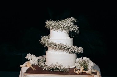 Taze beyaz çiçeklerle süslenmiş üç katlı bir düğün pastası. Geceleri dışarıda beyaz bir pasta duruyor. Güzel beyaz bir pasta küçük beyaz çiçeklerle süslenir..