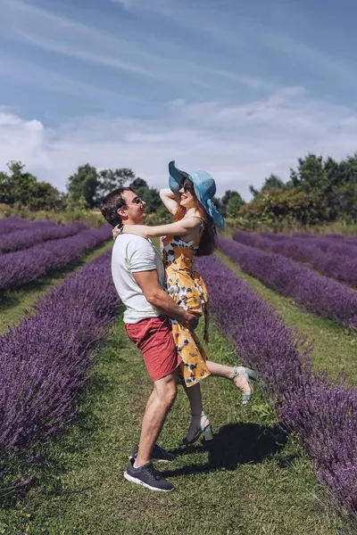 A couple in love, a man and a woman, are walking in a lavender meadow. The man lifted the woman in his arms, they look at each other and smile. A summer walk of a young couple through a lavender field