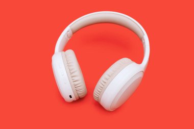 Parlak turuncu arka planda beyaz kablosuz bluetooth kulaklık. Oyun oynamak ve müzik dinlemek için tek kablosuz kulaklıklar. Kablosuz kulak kesme yolu olan kulaklıklar. Müzik konsepti