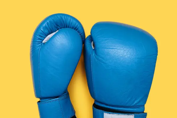 Blue boxing gloves isolated on yellow background. A pair of blue leather boxing gloves close-up top view. Boxing accessories