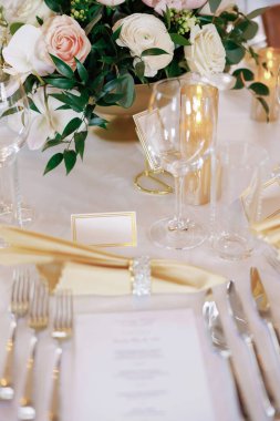 Masa düzenleri ve çiçek süslemeleri olan bir restoranda güzel dekore edilmiş bir masa. Bir restoranda lüks bir şekilde dekore edilmiş bir masa. Gümüş çatal bıçak, çiçekler ve temiz bardaklar masayı süsleyin.