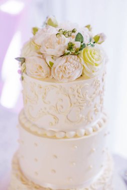 Gelin ve damadın düğün yemeği için güllerle süslenmiş üç katlı beyaz pasta. Lüks bir doğum günü pastası Bir restoranın masasında, üst manzara