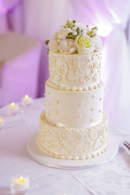 Gelin ve damadın düğün yemeği için güllerle süslenmiş üç katlı beyaz pasta. Lokantadaki bir masada lüks bir doğum günü pastası.