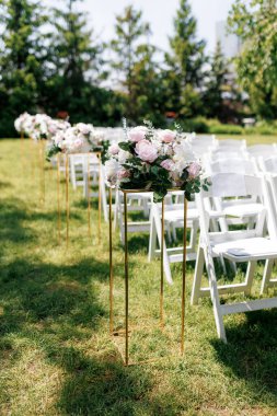 Davetliler için sandalye şeklinde bir düğün dekorasyonu ve tribünde çiçekler. Yeşil çimenlikteki misafirler için beyaz sandalyeler. Düğün töreni için mekanı hazırlıyorum.