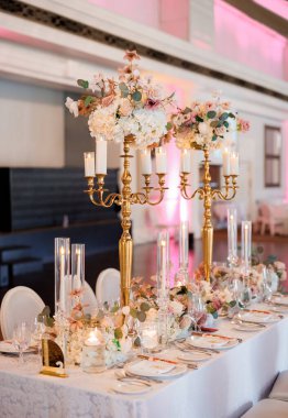 Restoranda altın şamdanlar ve çiçeklerle süslenmiş gelin ve damadın masası. Gelin ve damadın masası altın şamdanlar ve farklı çiçeklerle süslenmiş.