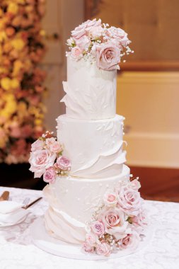 Pembe güllerle süslenmiş beyaz lüks pasta. Çok katmanlı güzel düğün pastası restoranın masasında duruyor. Gelin ve damat için geleneksel düğün pastası. Pasta şeklinde hamur işi.
