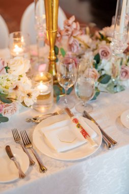 Çiçekler ve mumlarla süslenmiş bir restoranda güzel bir masa. Tabak ve çubuklu çatal bıçak takımı. Restoranda misafirleri bekleyen güzel bir masa.