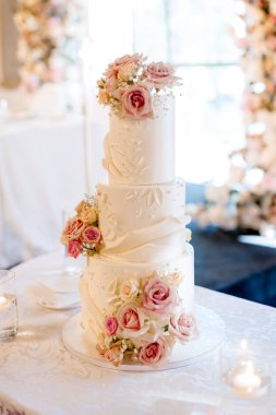 Pembe güller ve desenlerle süslenmiş beyaz lüks pasta. Çok katmanlı güzel düğün pastası restoranın masasında duruyor. Gelin ve damat için geleneksel düğün pastası