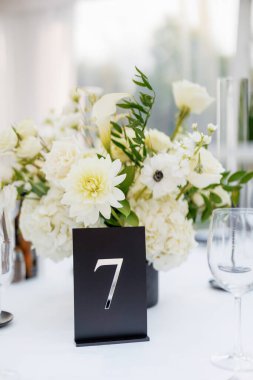 Yedi numaralı restorandaki rezerve masa çiçeklerle çevrili. Restorandaki masa numarası yakın plan. Beyaz çiçeklerle süslenmiş bir masa. Yedi numaralı masa.