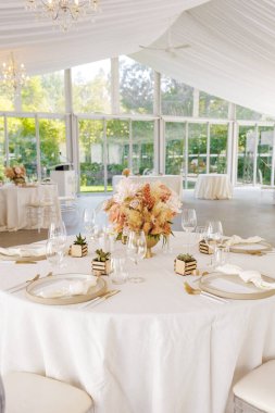 Çiçek düzenlemeleri, kaktüsler ve beyaz masa örtüleriyle süslenmiş zarif bir düğün kutlaması. İnsanlar olmadan düğün davetlileri için yuvarlak masalar hazırlayın.