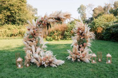 Çimlerin üzerinde kurumuş çiçekler ve güllerle süslenmiş yuvarlak düğün kemeri. Boho tarzında güzel yuvarlak bir düğün kemeri. Açık hava düğün töreni için dekorasyon.