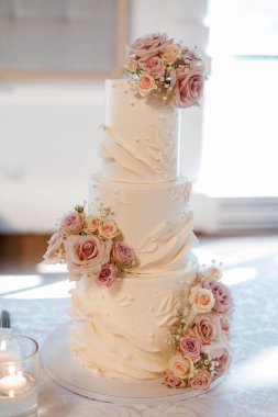 Pembe güller ve desenlerle süslenmiş beyaz lüks pasta. Çok katmanlı güzel düğün pastası restoranın masasında duruyor. Gelin ve damat için geleneksel düğün pastası