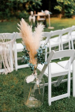 Açık hava düğün töreni için düğün süsleri. Kuru bitkiler ve okaliptüs bir cam şişe içinde beyaz boş sandalyelerin yanında bir düğün töreninde dekor olarak. Sözcük koltuğa ayrılmıştır.