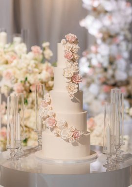Beş katlı beyaz düğün pastası. Arkaplanda güller ve çiçeklerle süslenmiş. Zarif bir uzun kremalı düğün pastası bir restoranda zarif beyaz ve pembe çiçeklerle süslenir.