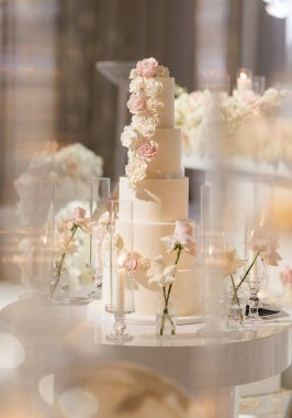 Restoranda büyük beyaz bir pastayla lüks bir düğün. Düğün süslemeleri pasta, çiçekler ve kapalı alanda dikey fotoğrafta yanan mumlar. Lezzetli ve çok katlı bir düğün pastası.