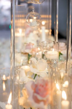 Törende cam mum tutacaklarında mum yakmak. Romantik ve duygusal bir ortam için gül ve mum süslemeleri. Yeni bir başlangıcın ya da vedanın sembolü olarak yanan mumlar