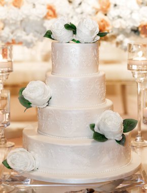Taze beyaz güllerle süslenmiş parlak jöleli düğün pastası. Masanın üzerinde dört katlı beyaz bir tatil pastası var. Yakın plan. Bir restoranda romantik bir ortamda nefis bir düğün pastası.