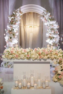 Beyaz kemerli, içinde bir sürü beyaz ve pembe gül bulunan lüks bir düğün resepsiyonu. Beyaz kemerlerin ve yanan mumların çiçek yerleştirilmesi düğünde romantik bir atmosfer yaratır.