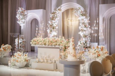 Beyaz renkli güzel çiçek aranjmanları olan lüks bir düğün dekorasyonu. Romantik bir ortam için bir sürü çiçeğin, kemerlerin ve yanan mumların olduğu bir düğün ziyafeti.