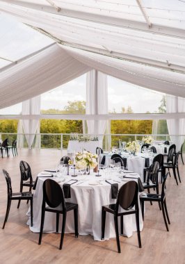 Açık bir verandada, kumaş tepe örtüsü olan bir restoranda çiçeklerle süslenmiş masalara servis yapardı. Gelin ve damadın onuruna bir ziyafet. Restoranda dikey fotoğraf var.