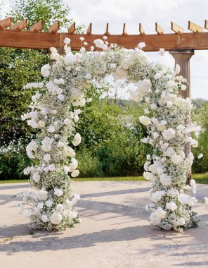Gelin ve damat için beyaz güllerle süslenmiş düğün kemeri. Beyaz çiçekli, düğün kemeri şeklinde bir dekorasyon. Gelin ve damadın düğün töreni için hazırlık.