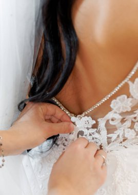 Gelini düğün gününe hazırlayan nedime ya da anne elbisesini bağlamasına yardım ediyor. Nedime gelinliğin arkasında yay düğümü yapıyor. Sabah hazırlığı. Gelinin törenden önceki sabahı