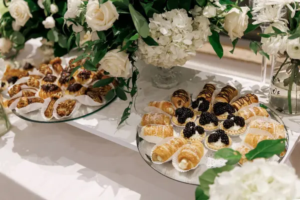 Düğün resepsiyonunda tatlı hamur işleri. Misafirler için seçebilecekleri ikramlar kapalı bir ziyafette çiçeklerle süslenmiş bir masanın üzerindeki tabaklar üzerinde sunuluyor. Şenlikli tatlı masası kavramı