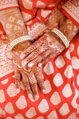 Kına ve altın mücevher ile boyanmış kadın elleri, kesilmiş fotoğraf. Mehendi ve bilezikler gelinin ellerinde parlak geleneksel bir elbisenin üzerinde, yakın plan. Hint geleneklerinde şenlik kıyafeti