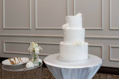 Beyaz vanilyalı kremayla kaplı çok katlı düğün pastası. Üç katlı düğün pastası yeni evliler tarafından kesilmeye hazır bir restoranda bir masanın üzerinde duruyor. Düğün ziyafetinde konuklar için tatlı.