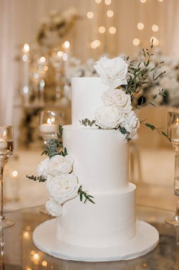 Resepsiyonda üç katlı güzel düğün pastası. Taze güllerle süslenmiş büyük beyaz kremalı düğün pastası. Restoranda zarif bir düğün tatlısı var.