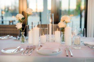 Beyaz masa örtülü servis masası, güller ve yanan mumlar romantik bir ortam yaratır. Düğündeki misafirler için bir masa çatal bıçaklı, mumlu, insansız. Düğün ziyafeti konsepti