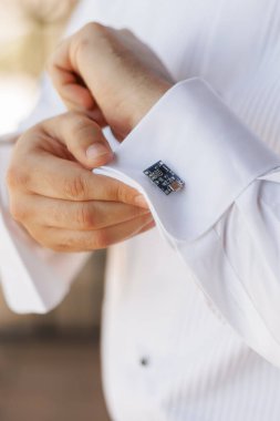 Beyaz gömlekli damat kol düğmeleri takıyor. Minyatür bilgisayar çipi şeklinde kol düğmeleri takan bir adamın ellerinin yakın çekimi. Temalı kol düğmeli adam özel bir etkinlik için hazırlanıyor.