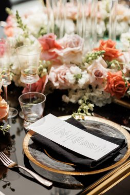 Bir kişi için zarif bir yemek masası. Tabak, çatal bıçak, bardak, peçete, menü ve çiçeklerle lüks bir ortam. Bir ziyafet, düğün, kutlama için güzel bir masa.