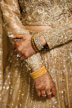 Karmaşık kına tasarımları, altın ve elmas bilezikler ve süslü bir elbise ile süslenmiş gelin elleri, geleneksel zarafet ve kültürel düğün mücevherleri sergileniyor.