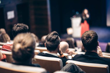 İş ve girişimcilik sempozyumu. İş toplantısında kadın konuşmacı bir konuşma yapıyor. Konferans salonunda dinleyiciler. İzleyicilerin tanınmayan katılımcılarının arka görünümü.
