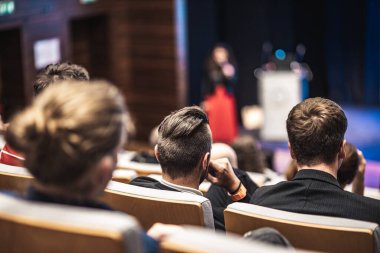 İş ve girişimcilik sempozyumu. İş toplantısında kadın konuşmacı bir konuşma yapıyor. Konferans salonunda dinleyiciler. İzleyicilerin tanınmayan katılımcılarının arka görünümü.