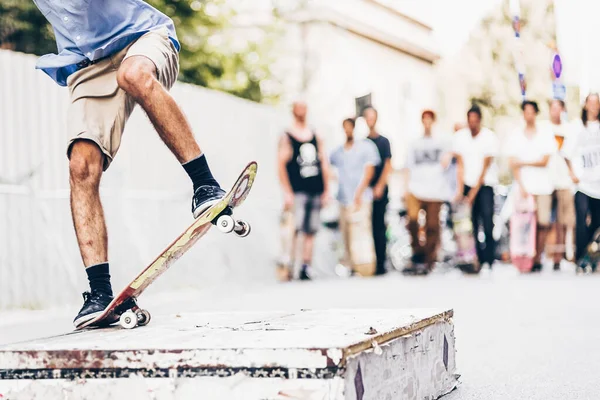 Young skateboarder skateboarding on the street. Skateboarding legs doing slide trick on object. Group of friends cheering in the background.