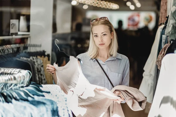 Woman shopping clothes. Female shopper looking at fashionable clothes indoors in clothing store.