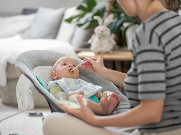母亲用勺子在婴儿椅上用果冻喂男婴 婴儿固体食物介绍概念 — 图库照片