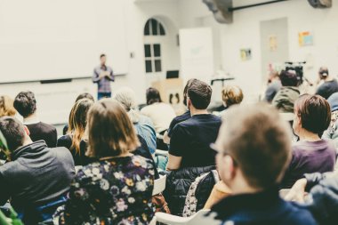 Üniversite atölyesindeki konferans salonunda erkek konuşmacı sunumu yapıyor. Konferans salonunda dinleyiciler. Seyircilerin tanınmayan katılımcılarının arka görüşü. Bilimsel konferans olayı.