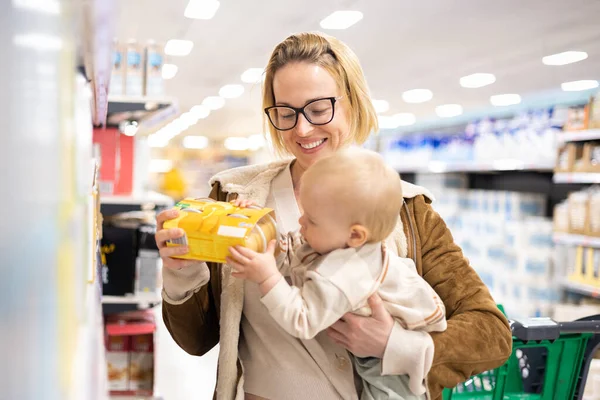 Caucasian mother shopping with her infant baby boy child choosing products in department of supermarket grocery store