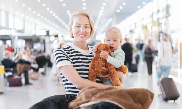 母親は子供と一緒に旅行し 空港ターミナルで飛行機に乗るのを待っている彼の幼児の男の子を抱いています 子供と一緒に旅行するコンセプト — ストック写真