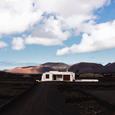 Traditional white house in black volcanic landscape of La Geria wine growing region with view of Timanfaya National Park in Lanzarote. Touristic attraction in Lanzarote island, Canary Islands, Spain