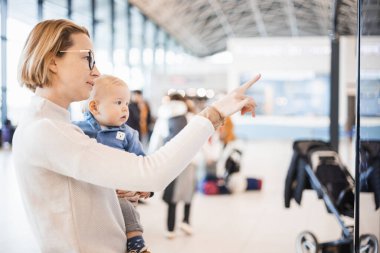 Anne çocuğuyla seyahat ediyor, bebeğini havaalanı terminalinde tutuyor uçuş saatlerini kontrol ediyor, uçağa binmeyi bekliyor. Çocuk konseptiyle seyahat