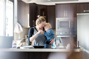 Mutlu anne ve küçük bebek çocuk ev mutfağında kahvaltı için krep yapıyorlar. Aile, yaşam tarzı, ev hayatı, yemek, sağlıklı beslenme ve insan kavramı