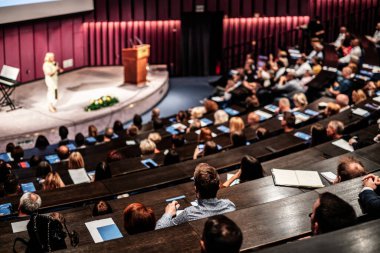 İş ve girişimcilik sempozyumu. İş toplantısında kadın konuşmacı bir konuşma yapıyor. Konferans salonunda dinleyiciler. İzleyicilerin tanınmayan katılımcılarının arka görünümü.
