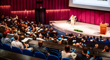 İş ve girişimcilik sempozyumu. İş toplantısında kadın konuşmacı bir konuşma yapıyor. Konferans salonunda dinleyiciler. İzleyicilerin tanınmayan katılımcılarının arka görünümü.