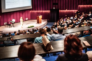İş ve girişimcilik sempozyumu. İş toplantısında kadın konuşmacı bir konuşma yapıyor. Konferans salonunda dinleyiciler. İzleyicilerin tanınmayan katılımcılarının arka görünümü.